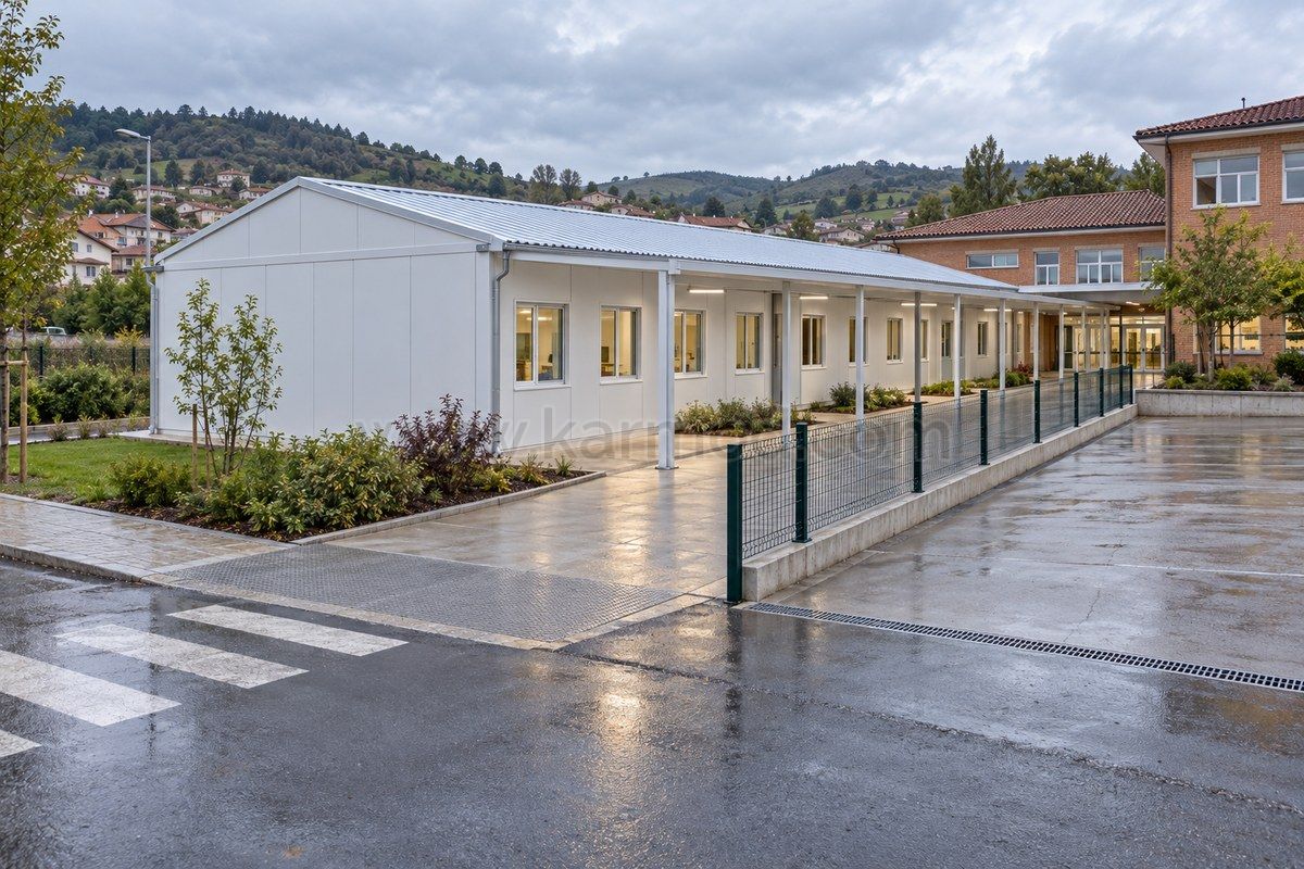 Accès à des classes modulaires par une galerie couverte, avec séparation entre le cheminement scolaire et la zone de livraison