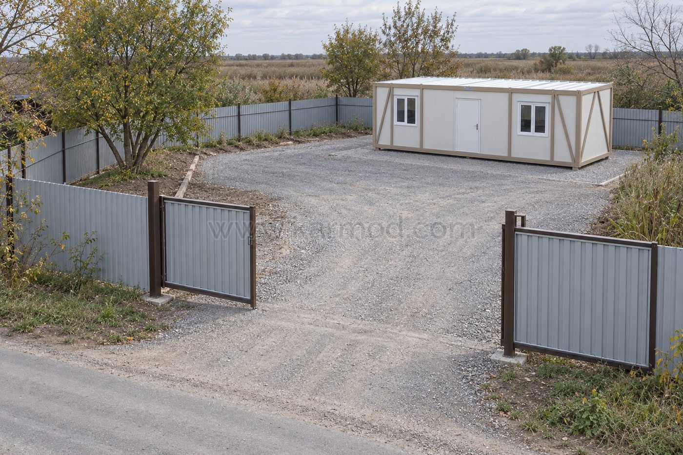 Блок-контейнер на огородженій ділянці з відкритими воротами та вільним гравійним під’їздом